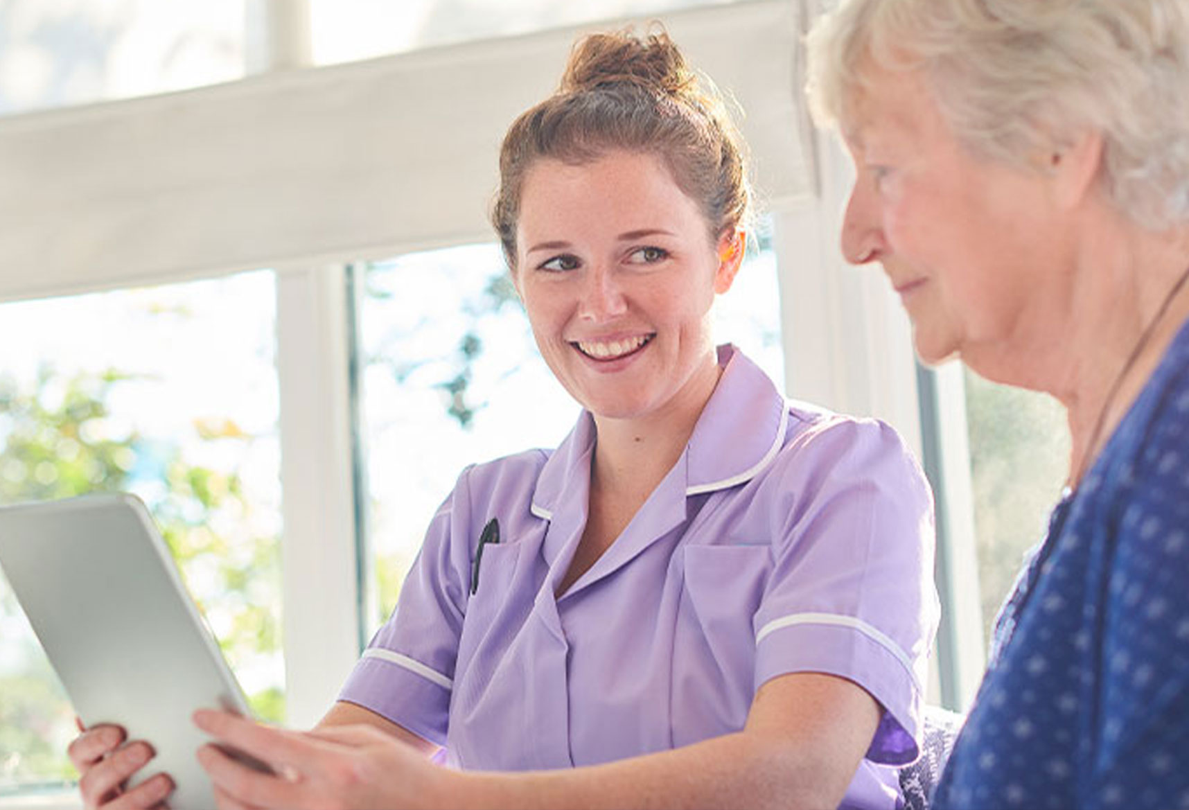 Female carer holding a tablet smiling at senior female resident