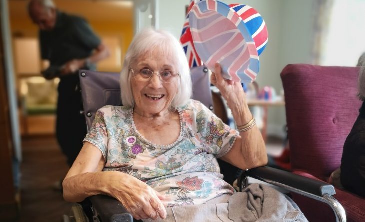Encore care homes resident in a wheelchair holding a union jack hat